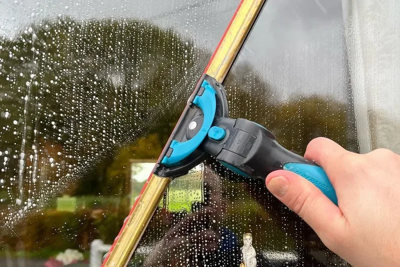Hand guiding a squeegee across a soapy window pane during a traditional window clean